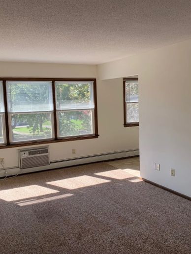 Empty carpeted room with large windows and an air conditioner.
