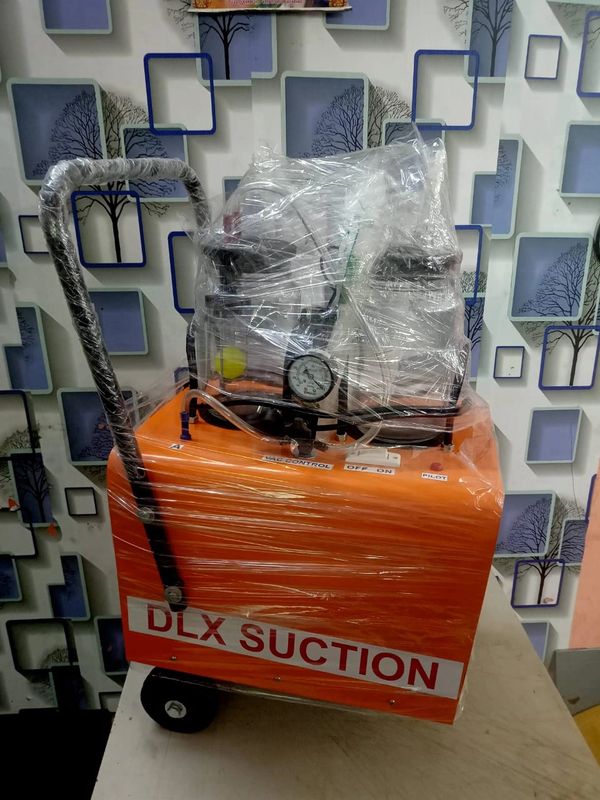 An orange DLX Suction machine wrapped in plastic on a table with a patterned wall background.