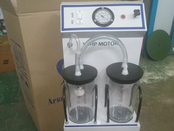 Medical suction machine with dual jars and pressure gauge on a green floor.