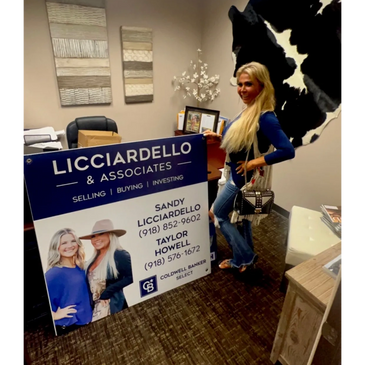 Woman posing with a real estate sign in an office.