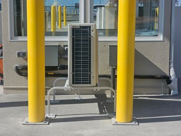 Outdoor air conditioning unit protected by yellow bollards.