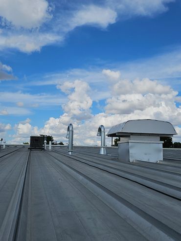 Metal rooftop with vents under a bright blue sky with fluffy clouds.