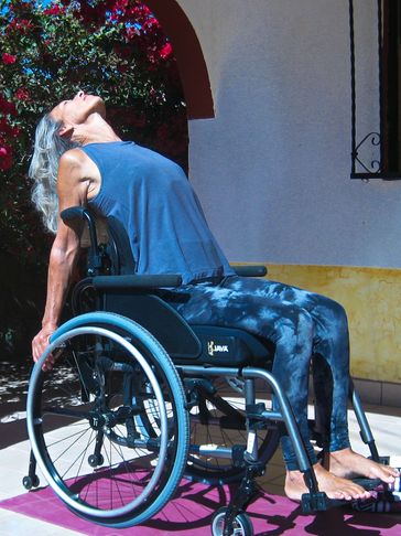 Seated in wheelchair with arms on the back of the wheels, back bend with heart lifted and head back.