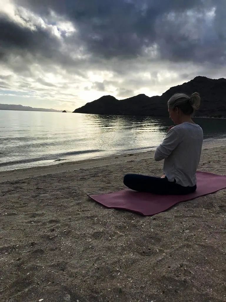 Seated on my yoga mat on the beach at sunrise with hands in Namaste, head bowed.