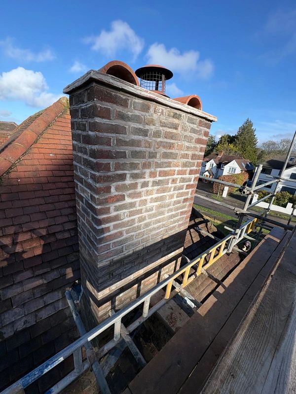 A newly rebuilt and repointed chimney on a tiled roof with scaffolding around it.