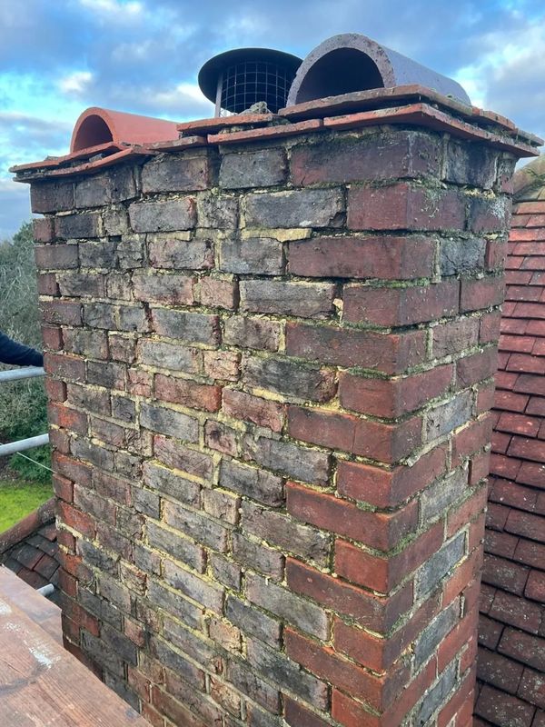 An old brick chimney with weathered and mossy bricks on a rooftop.