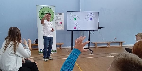 Instructor teaching sign language to kids in gym.