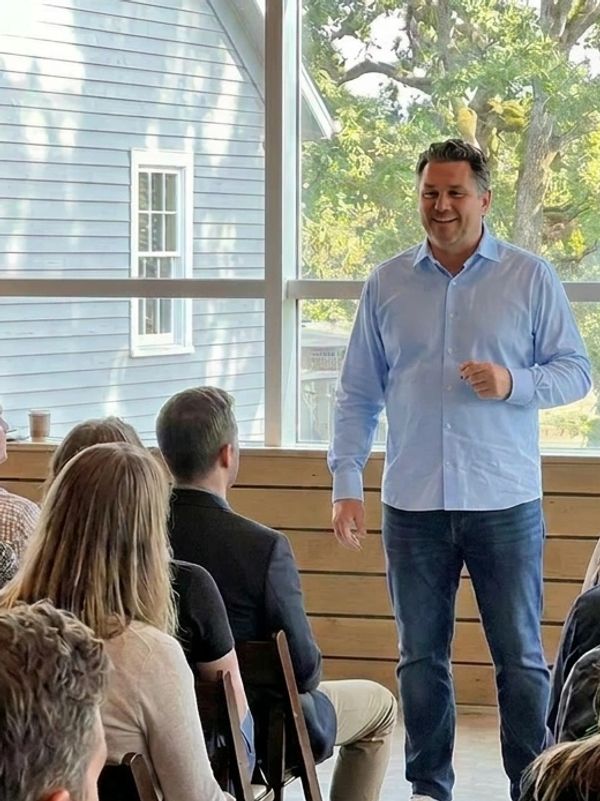 A man in a blue shirt speaking to an attentive audience indoors.