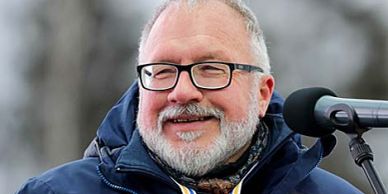Smiling older man with glasses speaking outdoors.