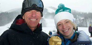 Two smiling people in winter gear with a snowy mountain in the background.