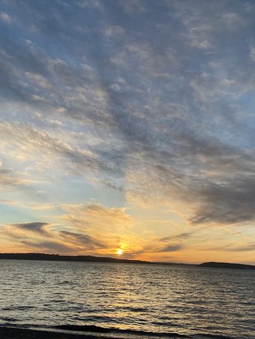 Sunset over a calm lake with scattered clouds.