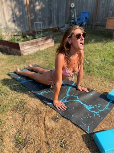 Woman in sunglasses doing yoga outdoors on a mat.