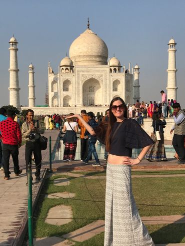 Tourist posing in front of the Taj Mahal on a sunny day.