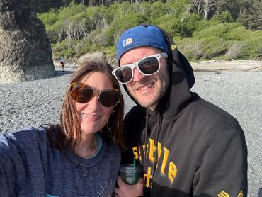 A happy couple wearing sunglasses at a rocky beach on a sunny day.