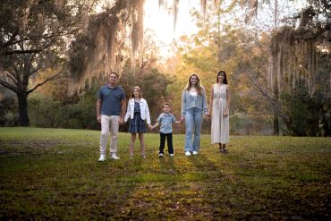 Family holding hands in a serene park at sunset.