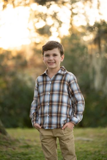 Smiling boy in plaid shirt outdoors during sunset.