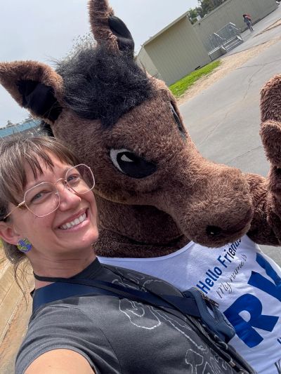 Person smiles next to horse mascot outdoors.