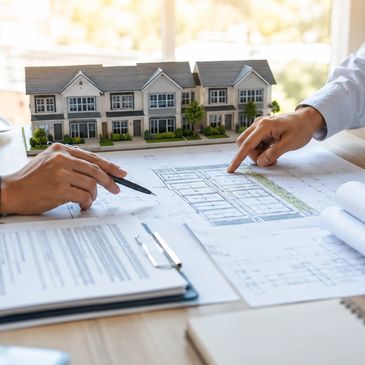 Two people reviewing architectural plans with a model house.