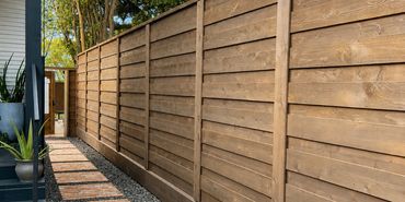 Stained horizontal cedar privacy fence with framed panels beside a brick walkway
