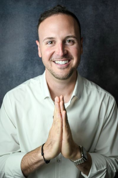Chase Skylar DeMayo smiling in a white shirt with his hands pressed together