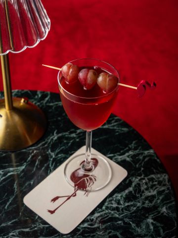 A red cocktail with grapes garnish on a marble table.