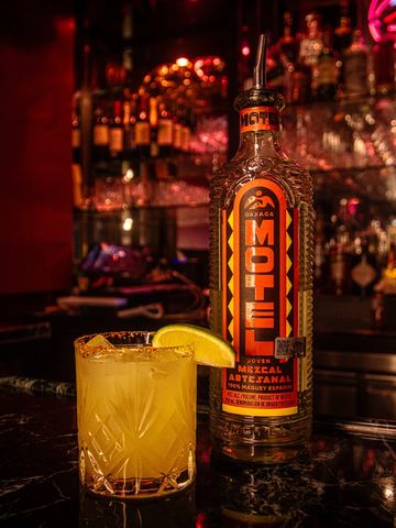 Bottle of Mezcal and a cocktail with a lemon garnish on a bar counter.