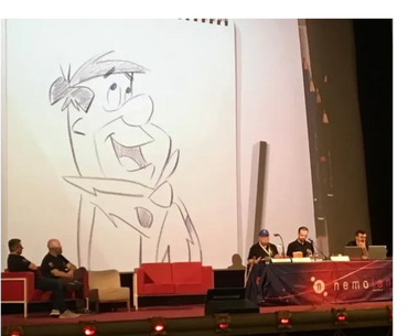 Panelists discuss animation with a large Fred Flintstone sketch projected behind them.