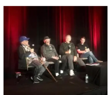 Four men seated on stage holding microphones during a panel discussion.