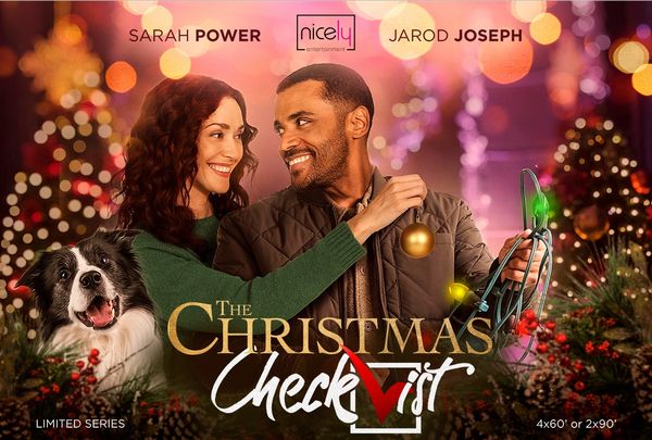 A couple smiling at each other with a dog and Christmas decorations.
