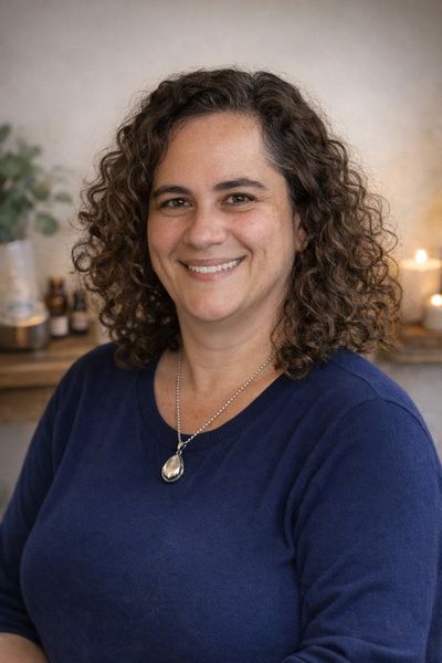 A smiling woman with curly hair wearing a blue top and a silver necklace.