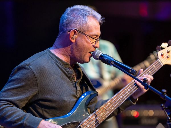Man passionately sings and plays bass guitar on stage under vibrant lights.