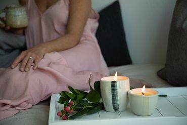 Woman in pink dress relaxing with lit candles and flowers on a tray.