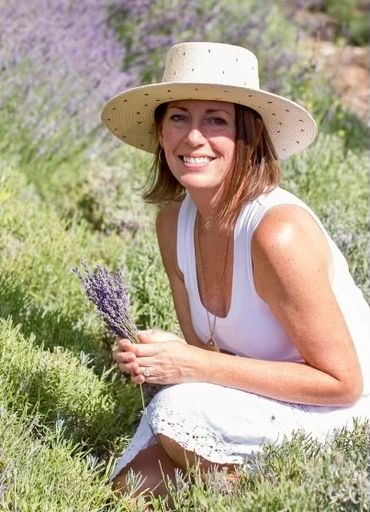 Woman in a white dress and hat holding lavender in a field.
