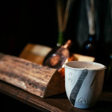 Ceramic candle holder with rustic wooden log and bottles in the background.
