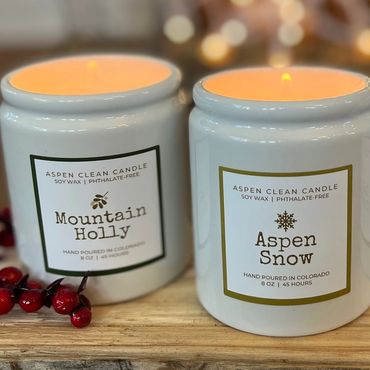 Three lit Aspen Clean candles with festive scents on a wooden surface.