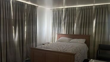 Cozy bedroom with a wooden bed, neutral curtains, and soft lighting.