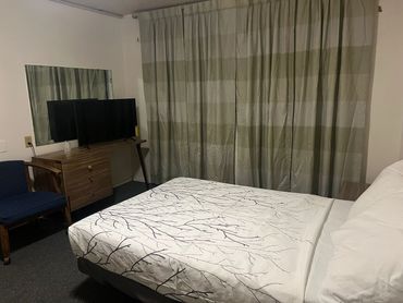 Simple bedroom with a bed, TV, striped curtains, and a blue chair.