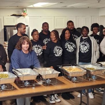 Group of people standing behind a buffet table in a kitchen.