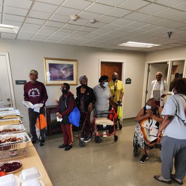 Group of elderly people gathered indoors near food trays.