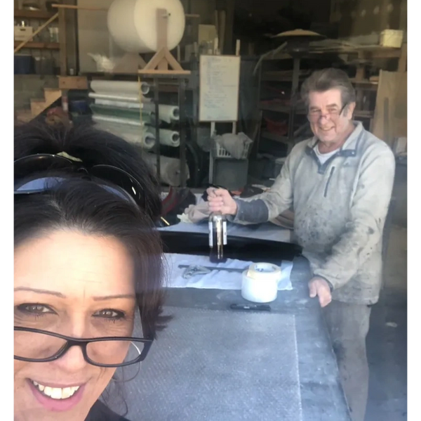 Two people smiling inside a workshop with materials and tools.