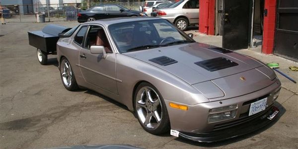 Silver Porsche 944 with custom rims parked outside a garage.