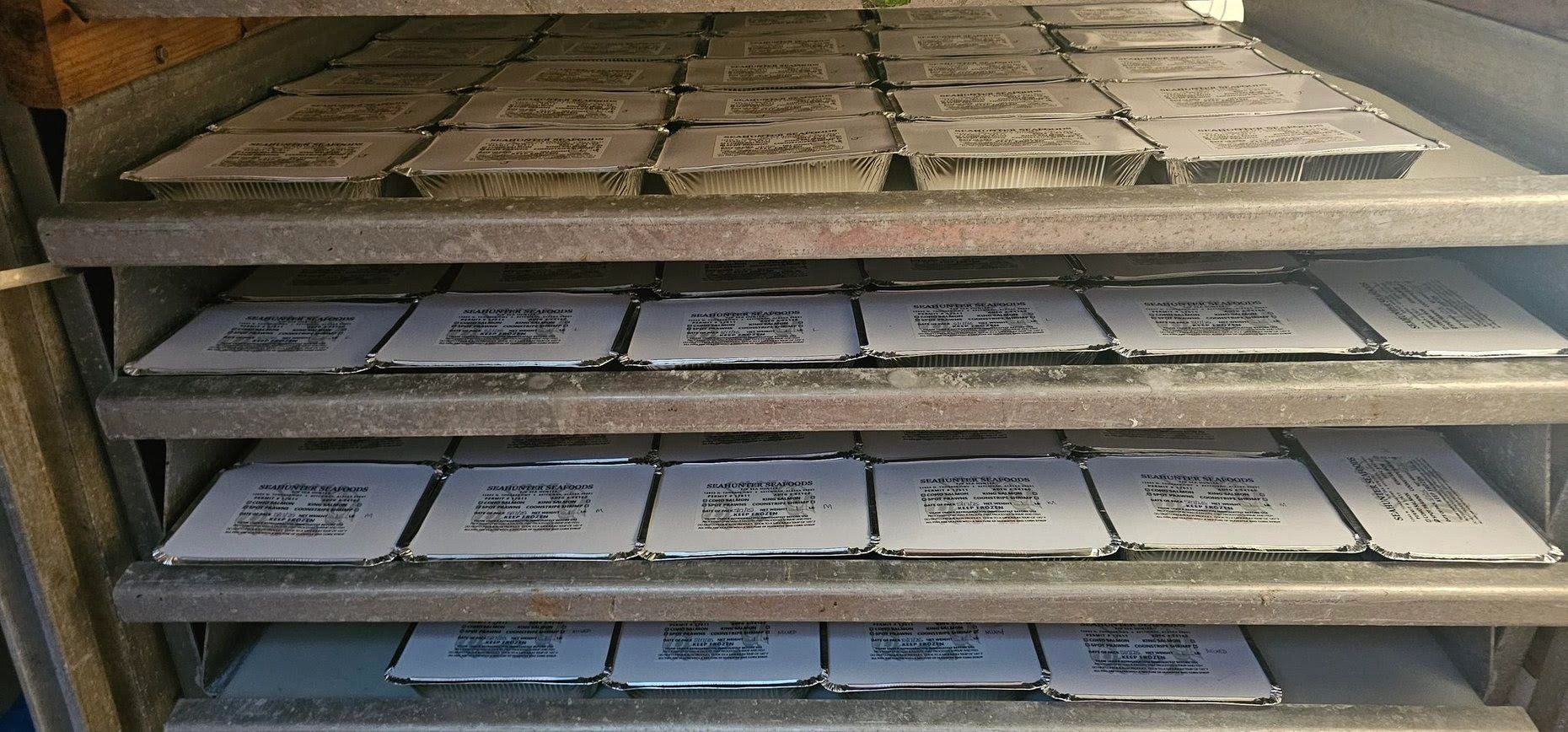 Several trays of sealed seafood containers stacked on metal shelves.