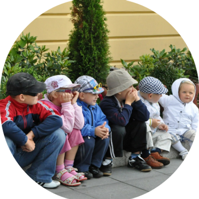 A group of young children sitting outdoors in a row, dressed warmly.