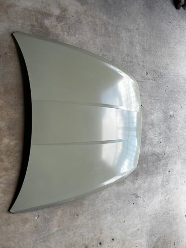 Car hood painted in a glossy light gray color on a concrete floor.