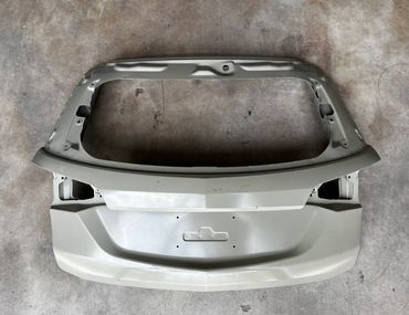 Unpainted car trunk lid placed on a concrete floor.