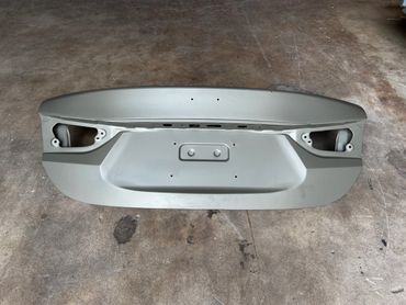 Unpainted car trunk lid placed on a concrete floor.