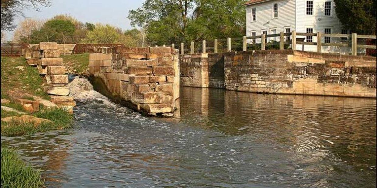 Historic stone canal lock with flowing water beside a white house.