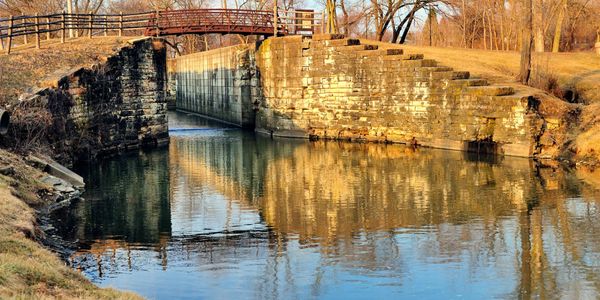A serene canal with stone walls and a wooden bridge in autumn.