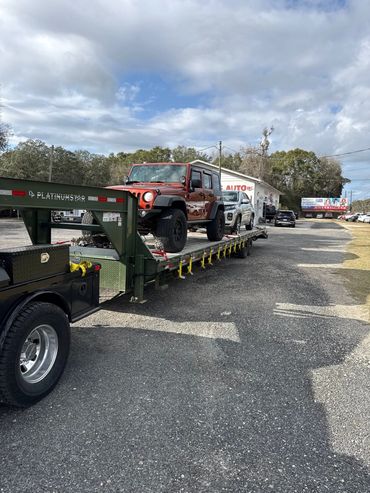 Two SUVs loaded on a PlatinumStar flatbed trailer under a partly cloudy sky.
