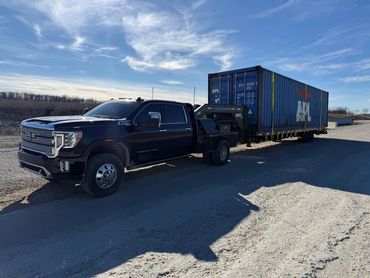 Black GMC Denali HD truck towing a blue shipping container on a sunny day.